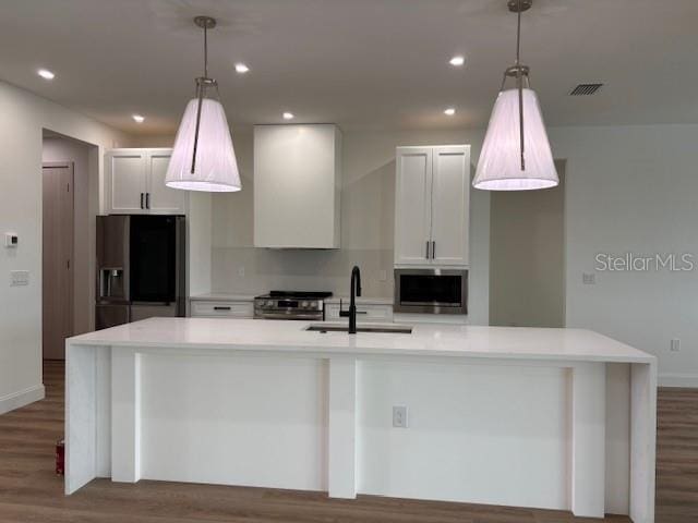 kitchen with appliances with stainless steel finishes, an island with sink, pendant lighting, white cabinets, and sink