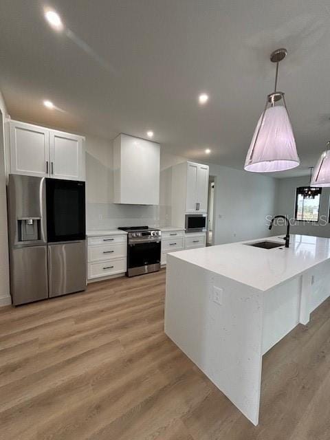 kitchen featuring light hardwood / wood-style flooring, decorative light fixtures, white cabinetry, appliances with stainless steel finishes, and sink