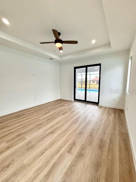 spare room featuring ceiling fan, a tray ceiling, and light hardwood / wood-style flooring