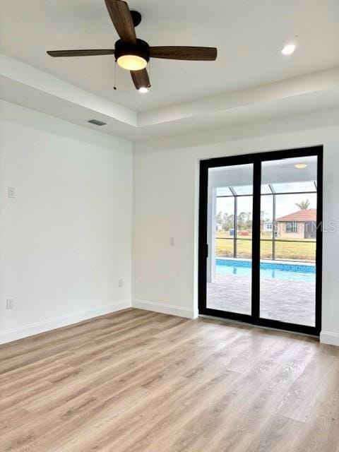 unfurnished room with a raised ceiling, ceiling fan, and light hardwood / wood-style floors