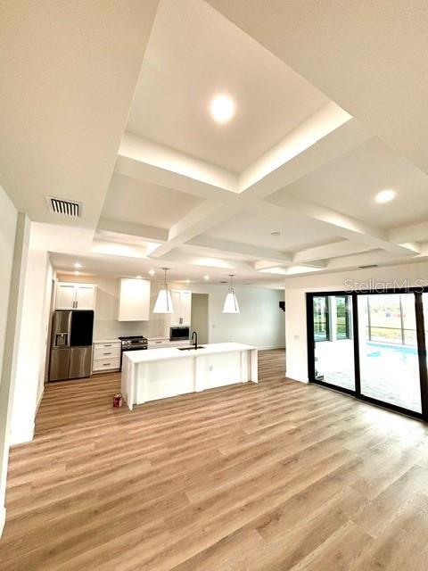 kitchen with sink, white cabinets, light hardwood / wood-style flooring, hanging light fixtures, and stainless steel refrigerator with ice dispenser