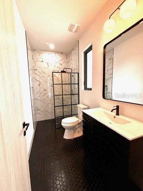 bathroom with a tile shower, vanity, and toilet