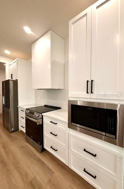 kitchen with stainless steel appliances, wood-type flooring, white cabinets, and wall chimney exhaust hood