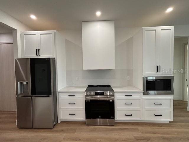 kitchen with white cabinetry, stainless steel appliances, decorative backsplash, wall chimney exhaust hood, and light hardwood / wood-style flooring