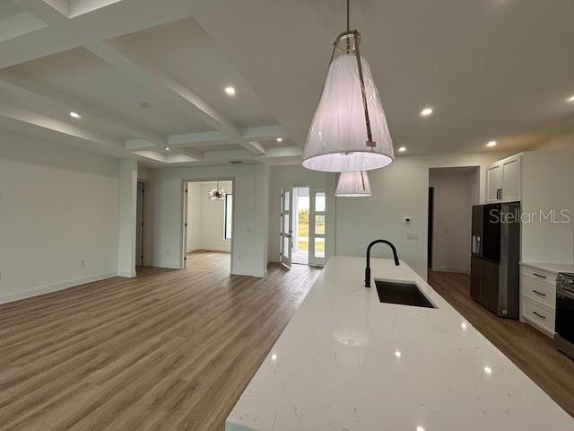 kitchen with sink, black fridge with ice dispenser, white cabinets, light stone countertops, and pendant lighting