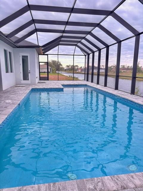 pool at dusk with a patio, a water view, and glass enclosure