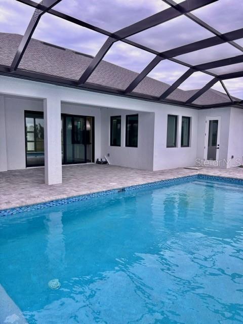 pool at dusk featuring a patio area and glass enclosure