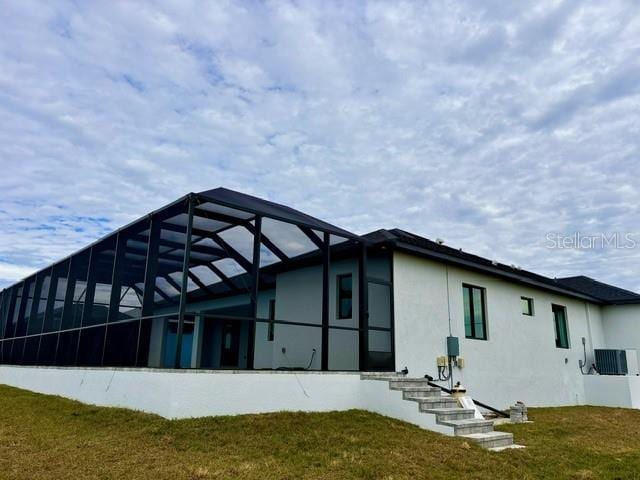 rear view of property with central air condition unit, a yard, and glass enclosure