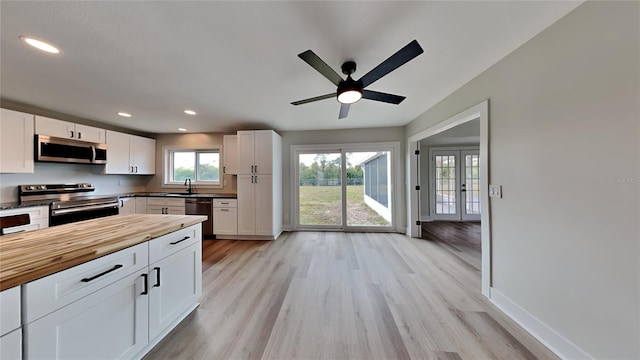 kitchen with stainless steel appliances, sink, white cabinets, ceiling fan, and light hardwood / wood-style floors