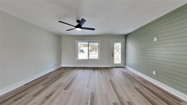 unfurnished room featuring ceiling fan, wooden walls, and light hardwood / wood-style flooring