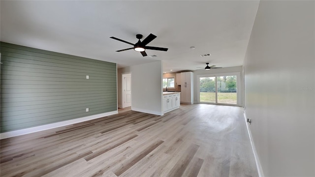 unfurnished living room with sink, wood walls, ceiling fan, and light hardwood / wood-style floors