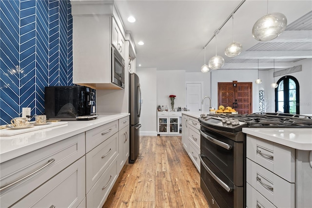 kitchen featuring hanging light fixtures, light hardwood / wood-style floors, white cabinetry, appliances with stainless steel finishes, and beamed ceiling