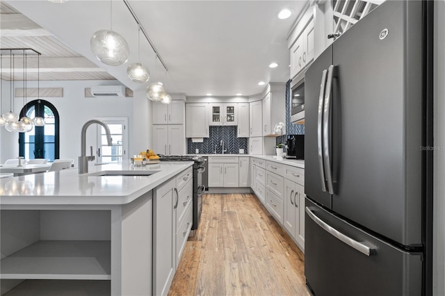 kitchen featuring an AC wall unit, a kitchen island with sink, backsplash, white cabinets, and appliances with stainless steel finishes