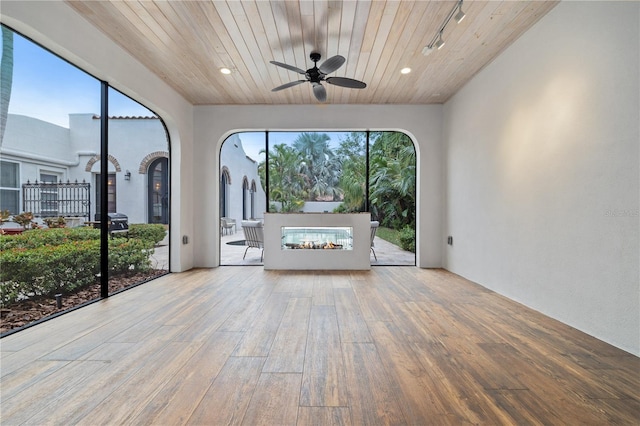 unfurnished sunroom featuring track lighting, a multi sided fireplace, wooden ceiling, and ceiling fan