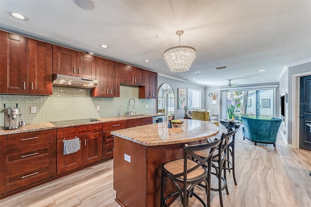 kitchen featuring light stone countertops, hanging light fixtures, a kitchen island, crown molding, and sink