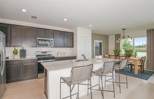 kitchen featuring sink, light tile patterned floors, a kitchen island with sink, stainless steel appliances, and decorative light fixtures