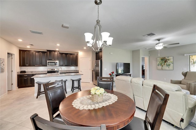 dining space featuring sink, light tile patterned flooring, and ceiling fan with notable chandelier