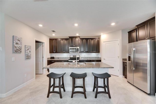 kitchen featuring sink, stainless steel appliances, a kitchen island with sink, and light stone counters