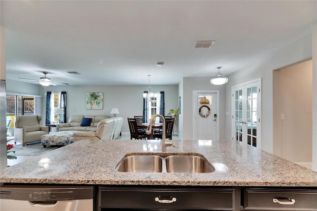 kitchen featuring an island with sink, light stone countertops, sink, decorative light fixtures, and stainless steel dishwasher