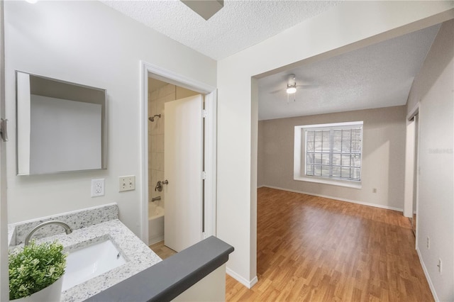 bathroom featuring wood-type flooring, ceiling fan, bathing tub / shower combination, a textured ceiling, and vanity