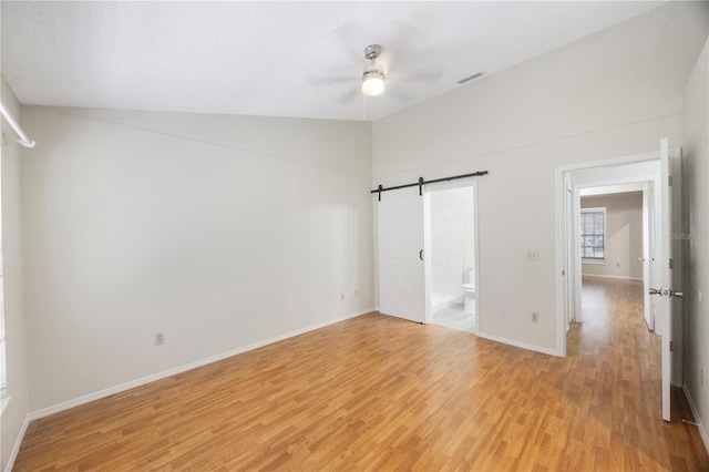 unfurnished bedroom with lofted ceiling, ceiling fan, ensuite bathroom, light hardwood / wood-style flooring, and a barn door