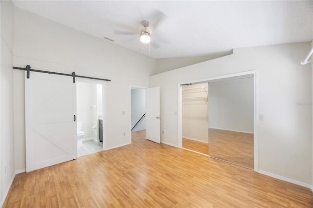 unfurnished bedroom with ceiling fan, a barn door, connected bathroom, light hardwood / wood-style floors, and a closet