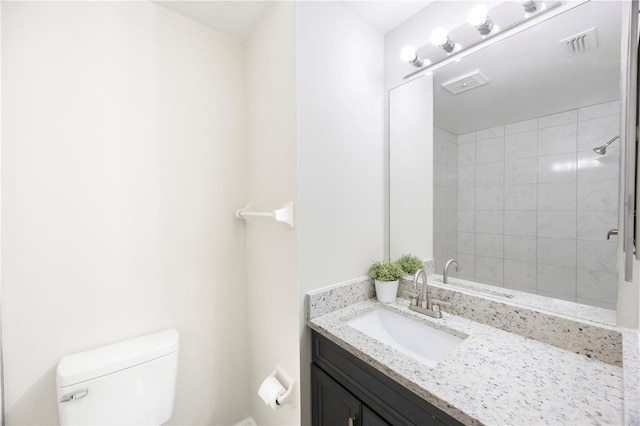 bathroom featuring toilet, vanity, and tiled shower