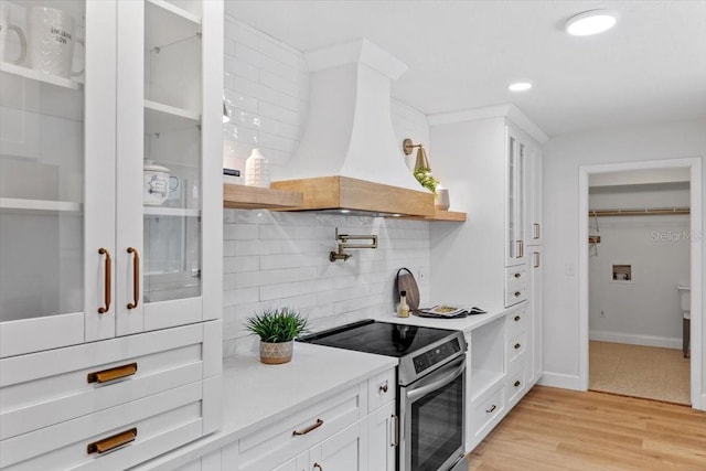 kitchen featuring stainless steel range with electric cooktop, light hardwood / wood-style floors, custom range hood, decorative backsplash, and white cabinets