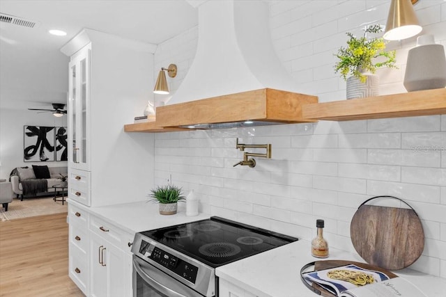 kitchen featuring white cabinetry, light hardwood / wood-style flooring, custom exhaust hood, decorative backsplash, and electric stove