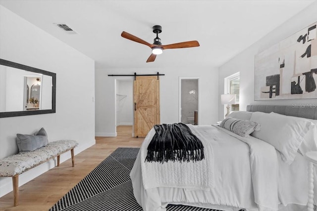 bedroom featuring ensuite bathroom, ceiling fan, light wood-type flooring, and a barn door