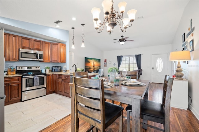 kitchen with appliances with stainless steel finishes, hanging light fixtures, light stone counters, vaulted ceiling, and light wood-type flooring