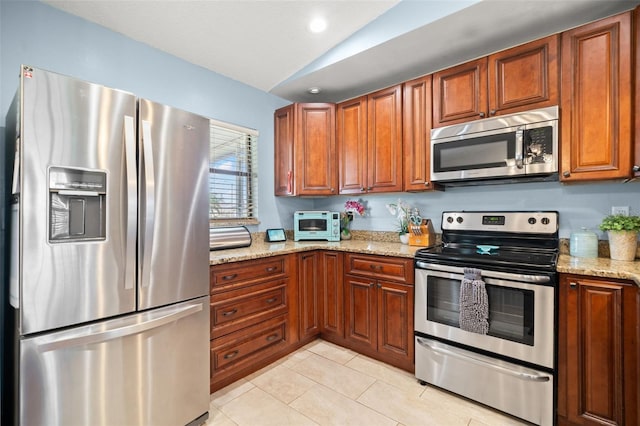 kitchen with stainless steel appliances, vaulted ceiling, light stone countertops, and light tile patterned floors