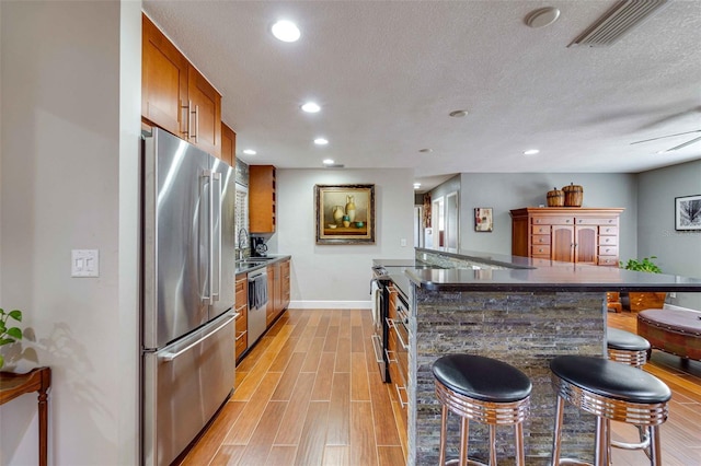 kitchen featuring stainless steel appliances, sink, a textured ceiling, ceiling fan, and a breakfast bar