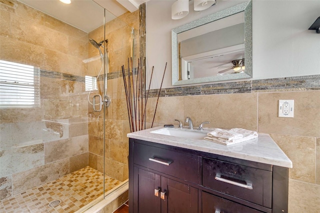 bathroom with tile walls, a shower with door, ceiling fan, and vanity