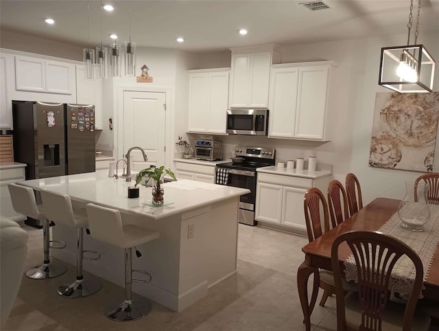 kitchen with an island with sink, appliances with stainless steel finishes, white cabinetry, and hanging light fixtures