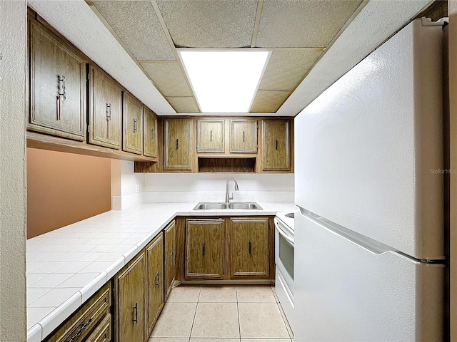 kitchen featuring sink, white appliances, tile countertops, and light tile patterned floors