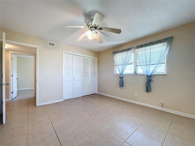 unfurnished bedroom featuring light tile patterned flooring, a textured ceiling, a closet, and ceiling fan