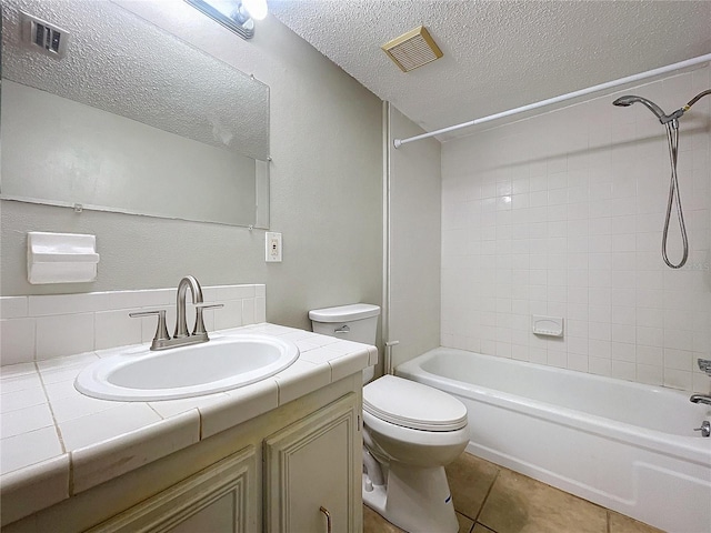 full bathroom with tile patterned flooring, tiled shower / bath combo, a textured ceiling, toilet, and vanity