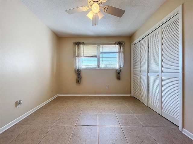 unfurnished bedroom with light tile patterned flooring, a textured ceiling, a closet, and ceiling fan