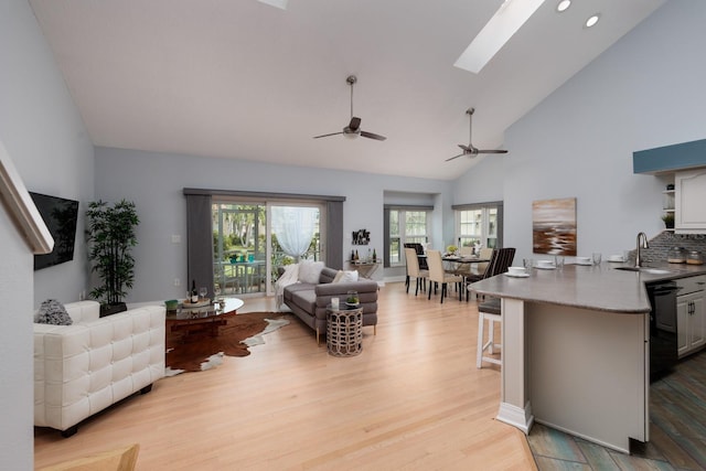 living room with sink, a skylight, high vaulted ceiling, light wood-type flooring, and ceiling fan