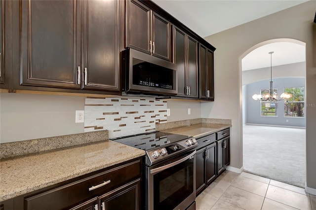 kitchen with dark brown cabinetry, stainless steel appliances, a chandelier, light stone counters, and light tile patterned floors