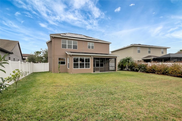 rear view of property featuring a lawn, solar panels, and a sunroom