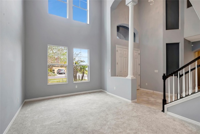 foyer entrance with ornate columns, light carpet, and a towering ceiling