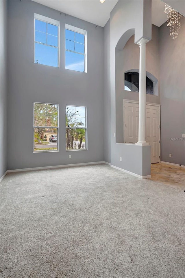 unfurnished living room featuring light colored carpet, a high ceiling, and ornate columns