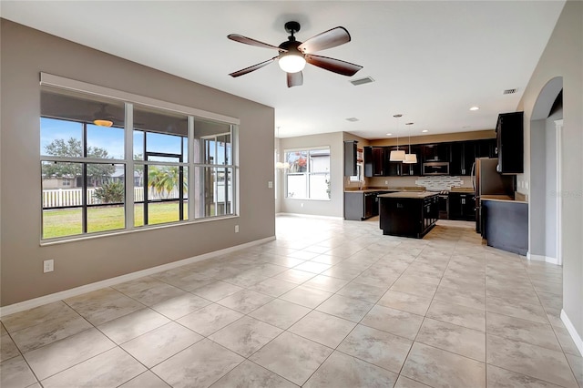 kitchen featuring ceiling fan, appliances with stainless steel finishes, decorative backsplash, decorative light fixtures, and a kitchen island