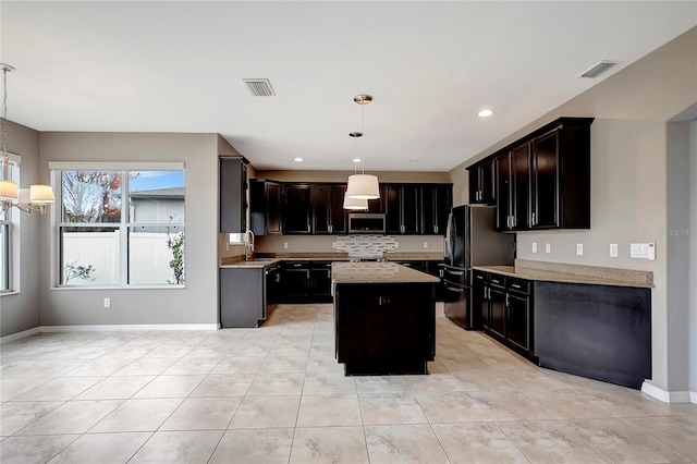 kitchen featuring black fridge, pendant lighting, a kitchen island, sink, and light stone countertops