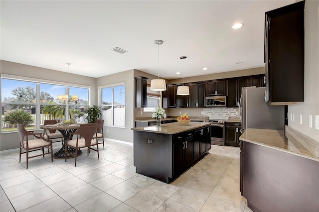 kitchen with appliances with stainless steel finishes, pendant lighting, a center island, and light stone countertops