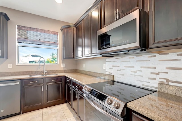 kitchen featuring light tile patterned floors, stainless steel appliances, light stone countertops, dark brown cabinetry, and sink