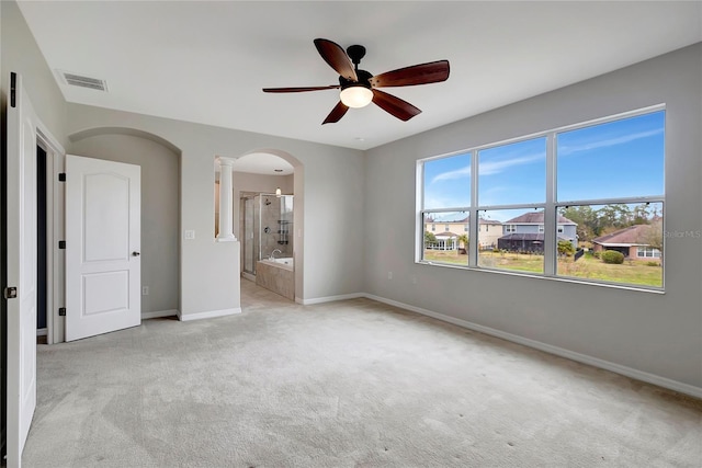 unfurnished bedroom with ceiling fan, ensuite bathroom, decorative columns, and light carpet