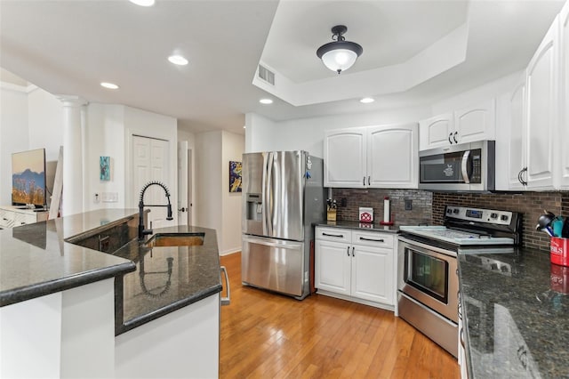 kitchen with stainless steel appliances, sink, white cabinets, tasteful backsplash, and dark stone counters